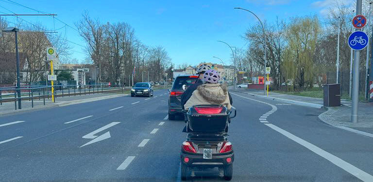 Senioren Elektromobil fährt auf Straße, Fahrer mit Helm